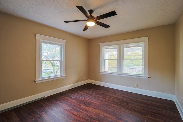 empty room with a textured ceiling, a healthy amount of sunlight, ceiling fan, and dark hardwood / wood-style flooring