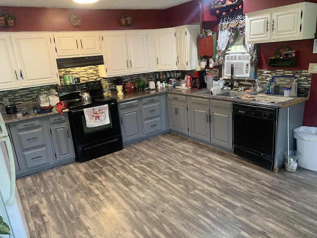 kitchen with wood finished floors, under cabinet range hood, gray cabinetry, black appliances, and a sink