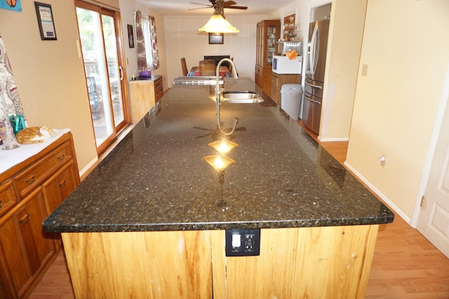 kitchen featuring stainless steel fridge, light hardwood / wood-style flooring, an island with sink, and ceiling fan