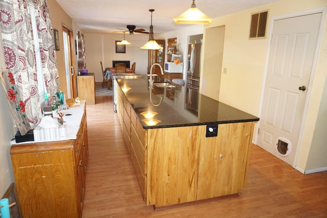 kitchen featuring stainless steel fridge, a center island with sink, light hardwood / wood-style flooring, hanging light fixtures, and sink