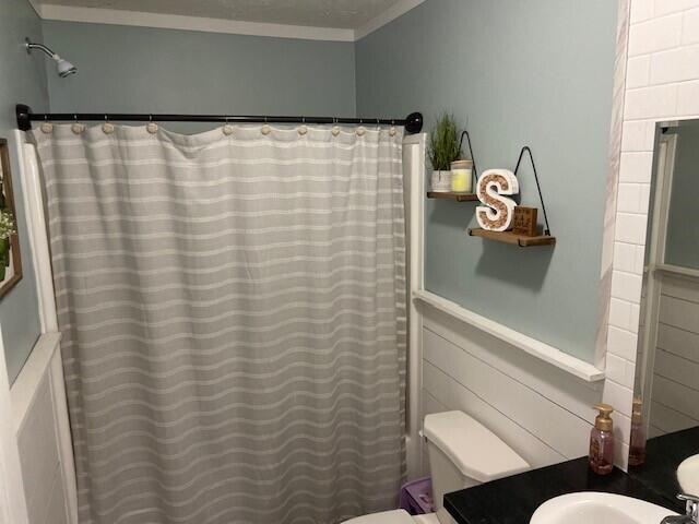 bathroom with a shower with curtain, crown molding, and toilet