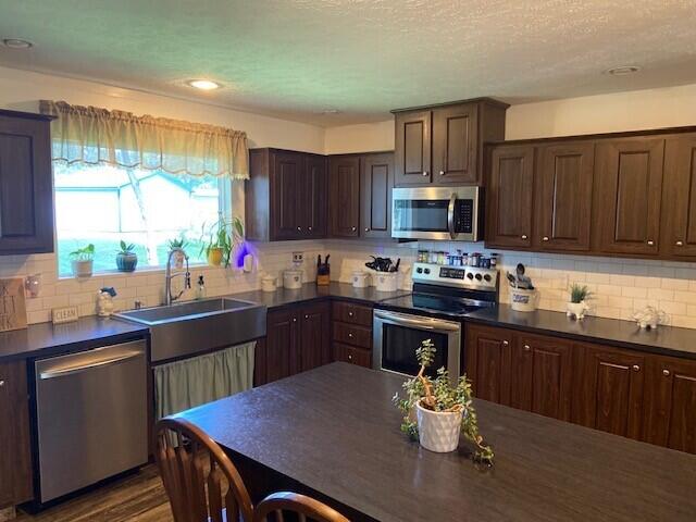 kitchen with tasteful backsplash, dark brown cabinets, sink, appliances with stainless steel finishes, and a textured ceiling