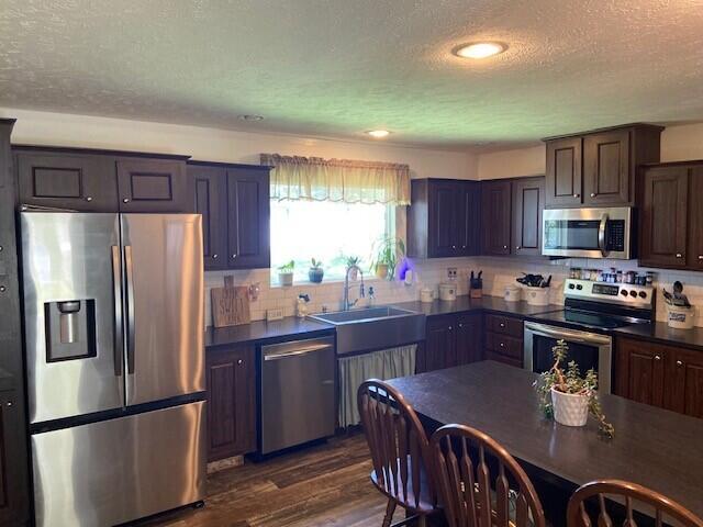 kitchen with dark hardwood / wood-style floors, stainless steel appliances, sink, dark brown cabinets, and a textured ceiling