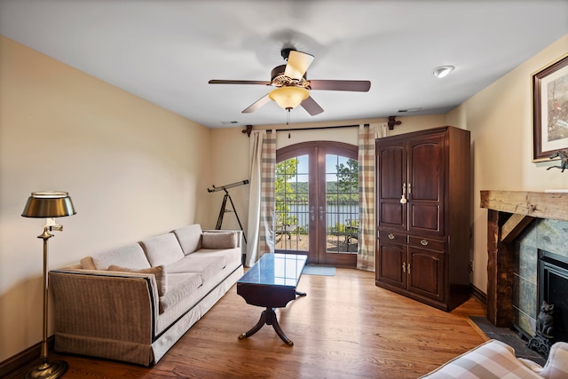 living room featuring ceiling fan, a fireplace, light wood-type flooring, and french doors