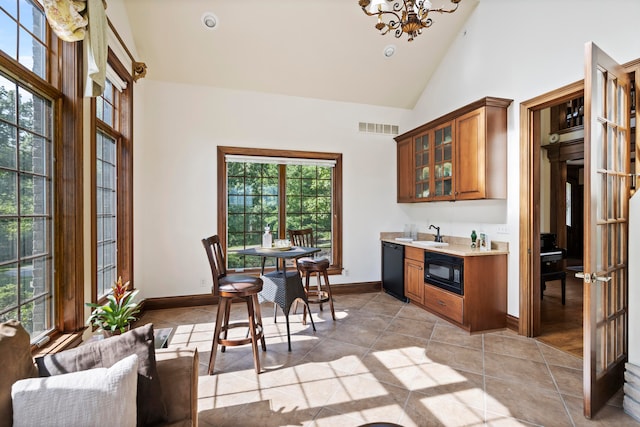 kitchen featuring light tile patterned flooring, high vaulted ceiling, black appliances, an inviting chandelier, and sink