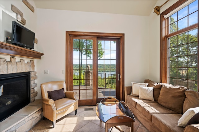 living room with a wealth of natural light, a water view, light tile patterned flooring, and a stone fireplace