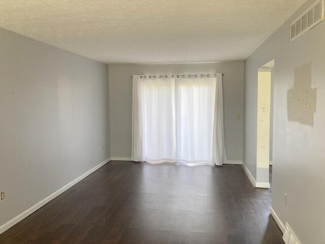 unfurnished room with a textured ceiling and dark wood-type flooring