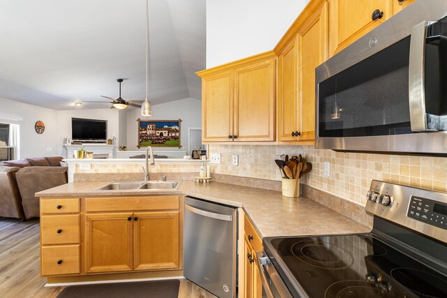 kitchen with sink, kitchen peninsula, light hardwood / wood-style floors, vaulted ceiling, and appliances with stainless steel finishes