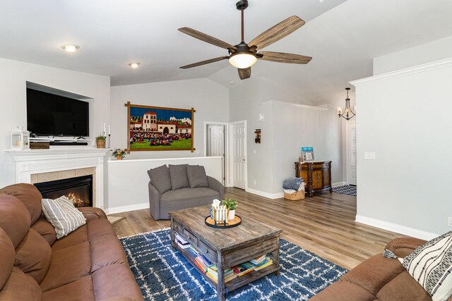 living room with a tiled fireplace, ceiling fan with notable chandelier, wood-type flooring, and vaulted ceiling