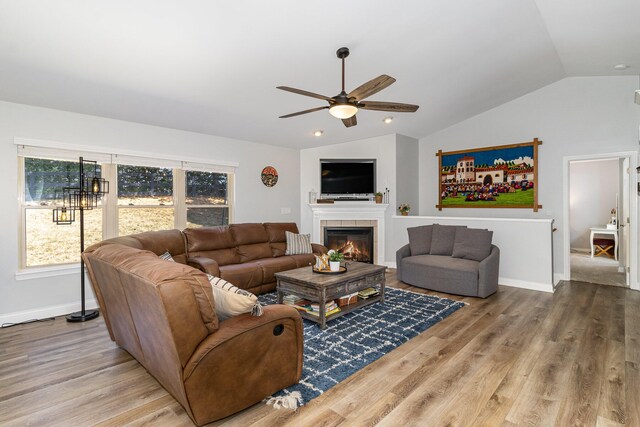 living room with ceiling fan, a fireplace, light hardwood / wood-style floors, and vaulted ceiling