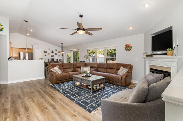 living room featuring wood-type flooring, vaulted ceiling, ceiling fan, and a tiled fireplace