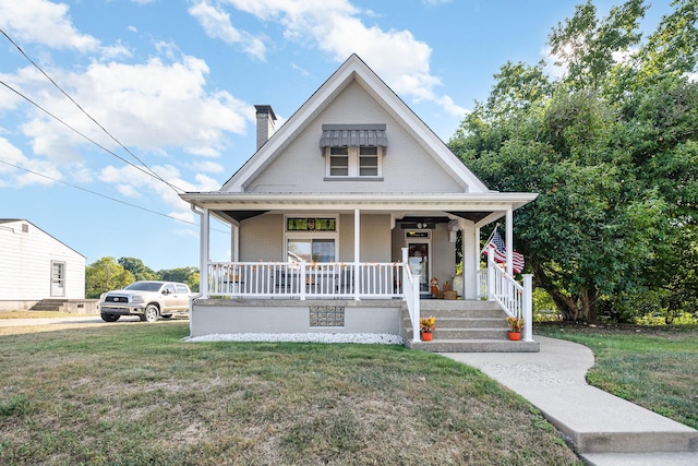 view of front facade featuring a chimney, brick siding, covered porch, and a front lawn