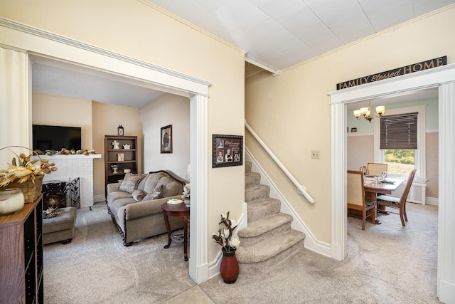 carpeted living area featuring ornamental molding, baseboards, a brick fireplace, a chandelier, and stairs