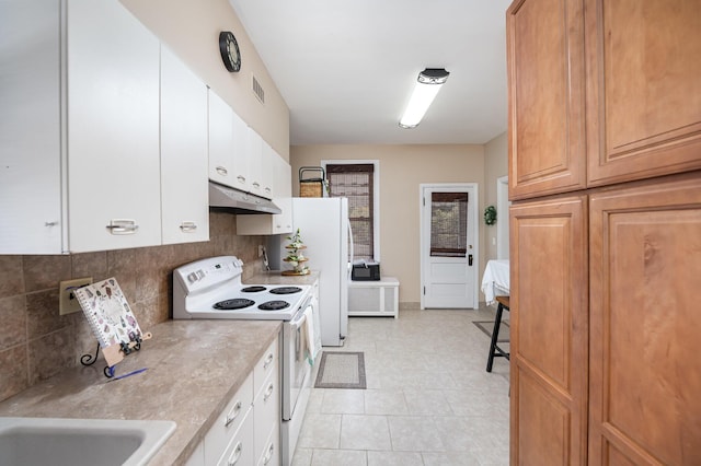 kitchen featuring under cabinet range hood, white appliances, white cabinets, light countertops, and decorative backsplash