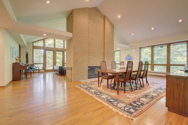 dining space with high vaulted ceiling, a wealth of natural light, light hardwood / wood-style flooring, and a fireplace