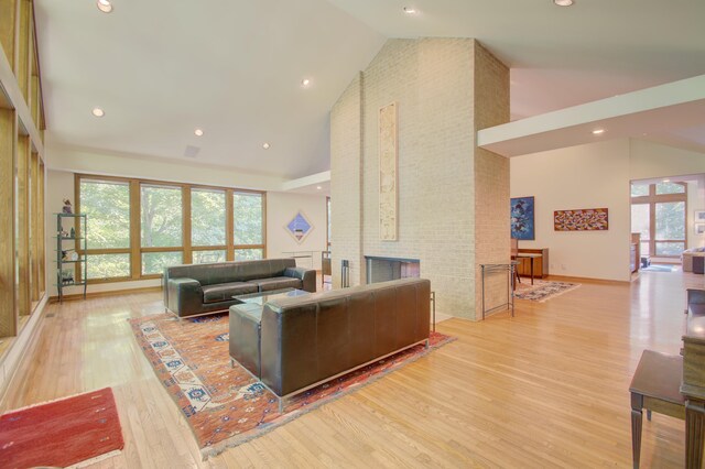 living room featuring high vaulted ceiling, a brick fireplace, and light hardwood / wood-style floors