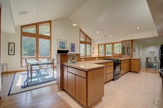 kitchen featuring light hardwood / wood-style floors, black gas range oven, high vaulted ceiling, kitchen peninsula, and pendant lighting