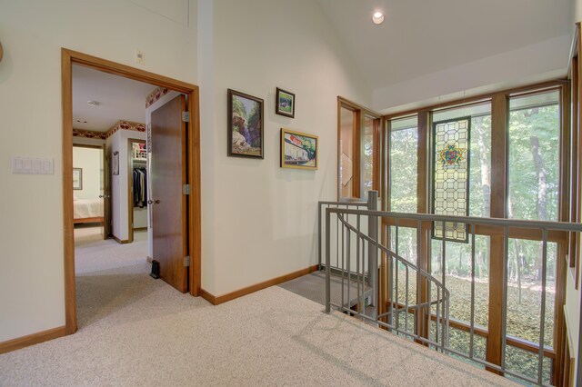 corridor with high vaulted ceiling, light carpet, and a wealth of natural light