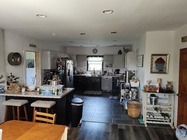 kitchen with gray cabinetry, appliances with stainless steel finishes, kitchen peninsula, dark wood-type flooring, and a kitchen bar