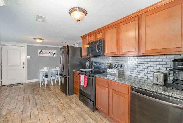 kitchen with dark stone countertops, ornamental molding, light hardwood / wood-style flooring, black appliances, and decorative backsplash