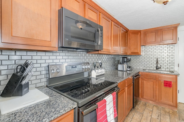 kitchen featuring a textured ceiling, appliances with stainless steel finishes, tasteful backsplash, sink, and dark stone counters