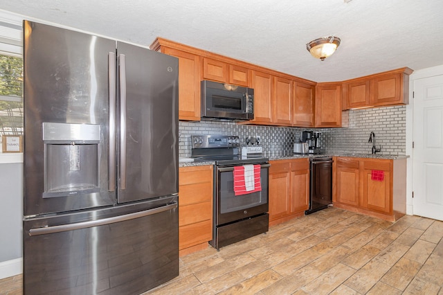 kitchen with backsplash, light wood-type flooring, light stone countertops, sink, and black appliances