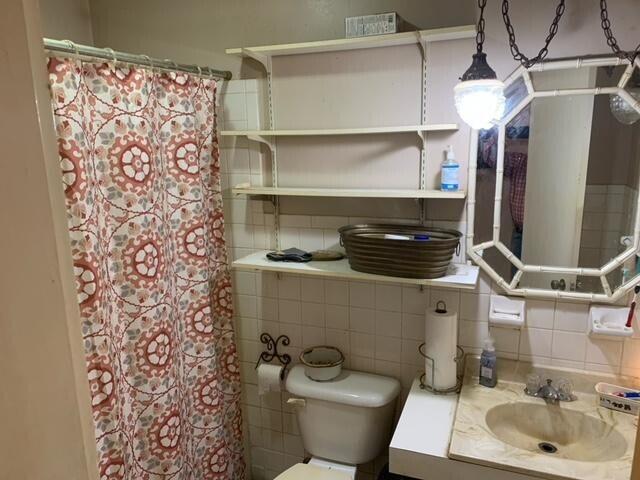 bathroom featuring backsplash, walk in shower, toilet, tile walls, and vanity