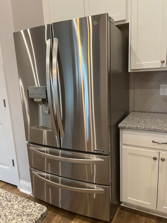 kitchen with backsplash, light stone counters, white cabinetry, stainless steel fridge, and dark hardwood / wood-style floors