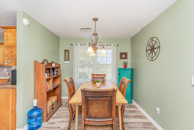 dining room featuring a textured ceiling, light hardwood / wood-style flooring, and an inviting chandelier