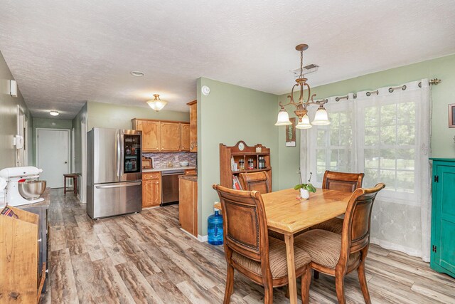 dining area featuring a textured ceiling, a notable chandelier, and light wood-type flooring