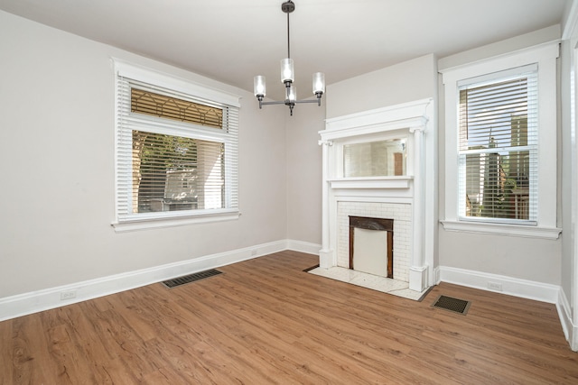 unfurnished living room featuring a fireplace, plenty of natural light, hardwood / wood-style flooring, and a notable chandelier