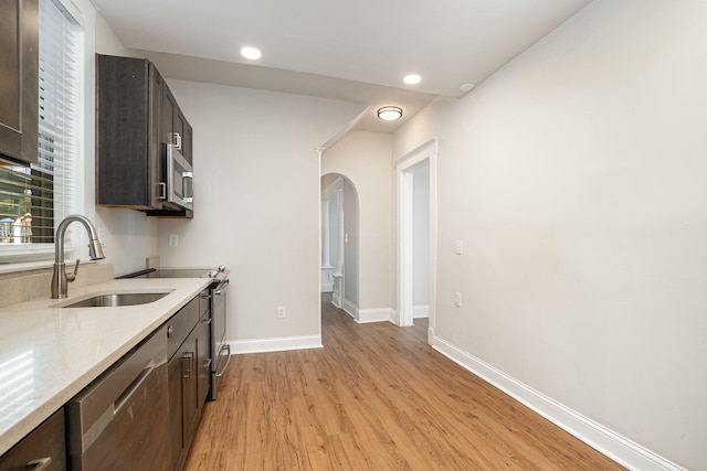 kitchen with light wood-type flooring, dark brown cabinets, sink, light stone countertops, and appliances with stainless steel finishes