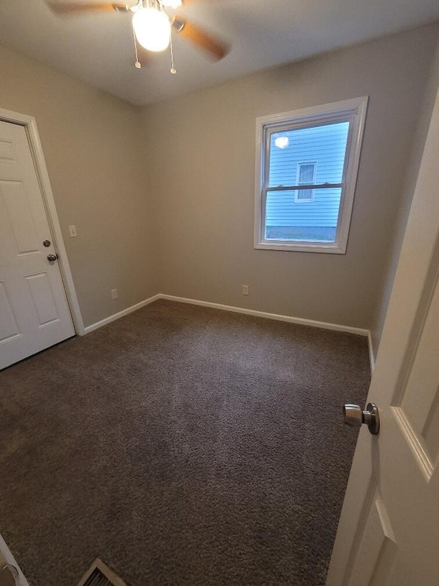 empty room with ceiling fan and dark colored carpet