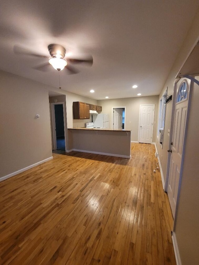 interior space with ceiling fan, kitchen peninsula, light hardwood / wood-style floors, and white fridge