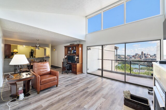 living room featuring ceiling fan, high vaulted ceiling, a textured ceiling, and light wood-type flooring