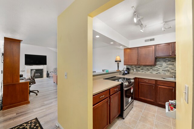 kitchen with kitchen peninsula, light wood-type flooring, tasteful backsplash, sink, and electric stove