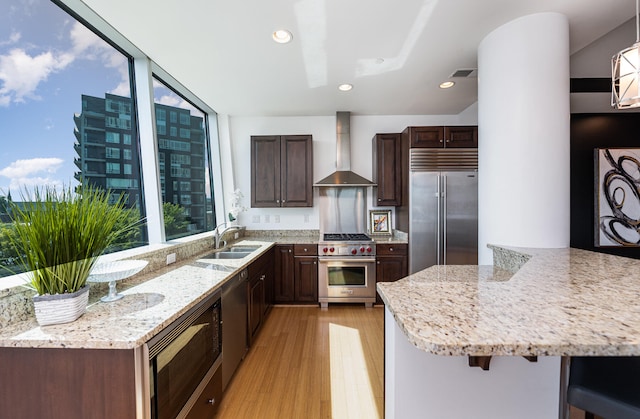 kitchen featuring sink, wall chimney range hood, built in appliances, a breakfast bar, and light hardwood / wood-style floors