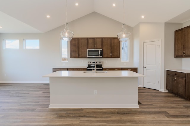 kitchen with hardwood / wood-style floors, appliances with stainless steel finishes, a kitchen island with sink, and hanging light fixtures