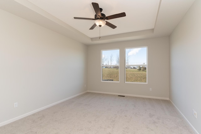 carpeted spare room with ceiling fan and a tray ceiling