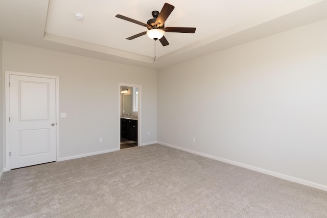 unfurnished bedroom with a raised ceiling, ceiling fan, carpet, and ensuite bath