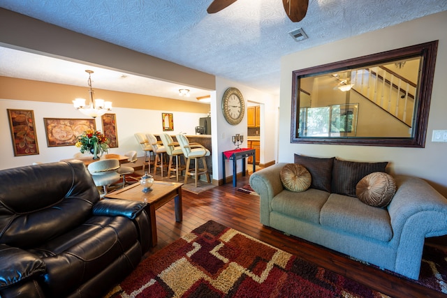 living room with ceiling fan with notable chandelier, dark wood-type flooring, and a textured ceiling