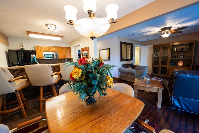 dining area with dark wood-type flooring, ceiling fan with notable chandelier, and a textured ceiling