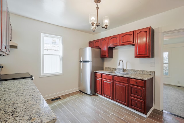 kitchen with a chandelier, sink, decorative light fixtures, light stone countertops, and stainless steel fridge