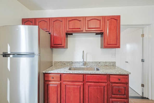 kitchen featuring light stone counters, sink, and stainless steel refrigerator