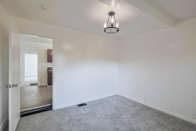 empty room with carpet flooring, beam ceiling, and an inviting chandelier