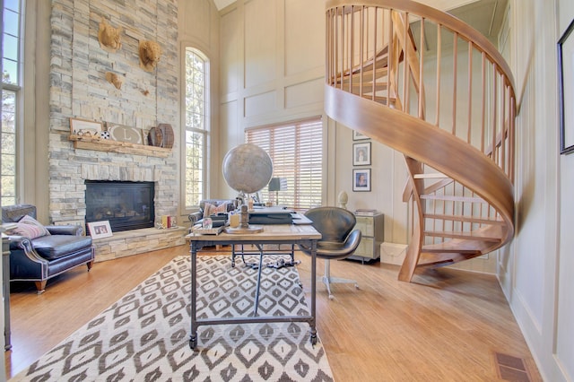 office area featuring light wood-type flooring, a towering ceiling, and a stone fireplace