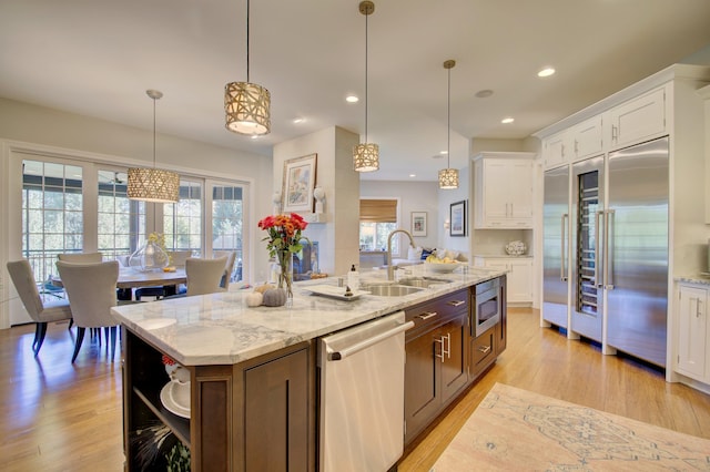 kitchen with white cabinets, an island with sink, built in appliances, and pendant lighting