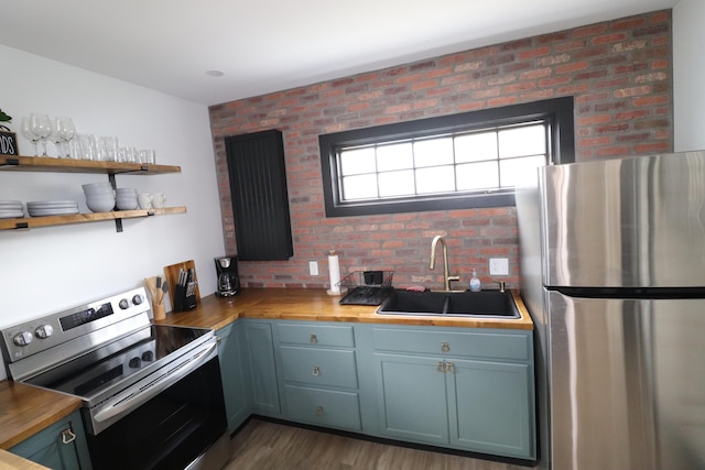 kitchen featuring appliances with stainless steel finishes, brick wall, dark hardwood / wood-style flooring, wooden counters, and sink