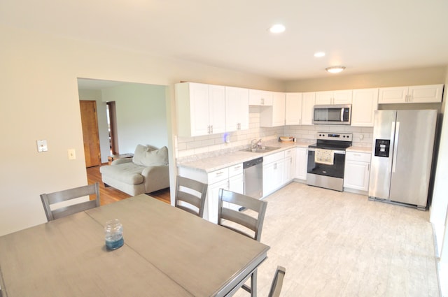 kitchen with decorative backsplash, white cabinets, stainless steel appliances, light hardwood / wood-style flooring, and sink