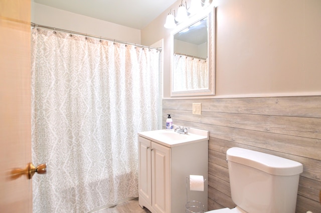 bathroom with walk in shower, wood walls, vanity, and toilet